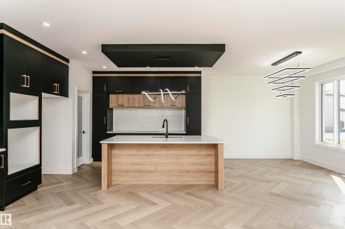 Two tone kitchen featuring dual tone cabinetry, pendant lighting, a kitchen island with sink, parquet flooring, and light stone countertops - 3248 Pelerin Crescent, Beaumont, AB - Indoor
