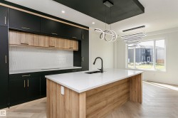 Kitchen featuring dual tone cabinets, parquet floors, light stone countertops, decorative light fixtures, and a center island with sink - 
