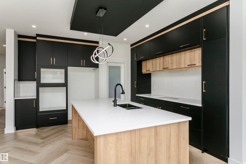 Two tone kitchen with two tone cabinetry, light stone countertops, parquet flooring, an island with sink, and hanging light fixtures - 3248 Pelerin Crescent, Beaumont, AB - Indoor Photo Showing Kitchen With Double Sink With Upgraded Kitchen