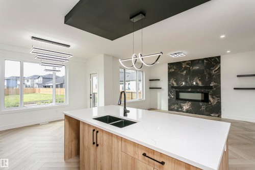 Kitchen featuring parquet floors, light wood finish cabinets, a center island with sink, light stone countertops, and open floor plan - 3248 Pelerin Crescent, Beaumont, AB - Indoor Photo Showing Other Room