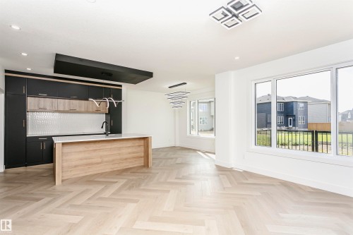 Kitchen featuring parquet flooring, two tone color scheme, a center island with sink, light stone counters, and recessed lighting - 3248 Pelerin Crescent, Beaumont, AB - Indoor