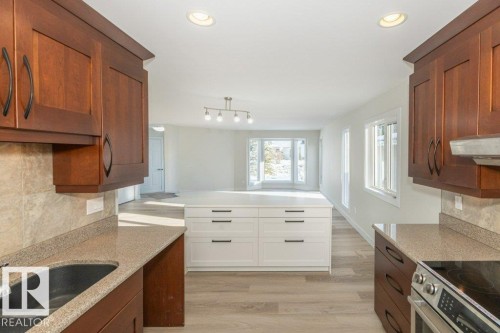 Dual tone kitchen featuring backsplash, two tone cabinetry, light wood-style flooring, stainless steel electric stove, and light stone counters - 5720 109A Street Nw, Edmonton, AB - Indoor Photo Showing Kitchen