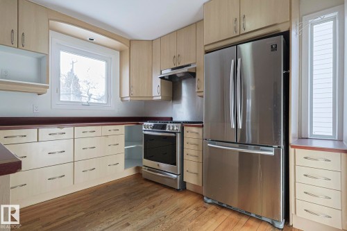 Kitchen featuring stainless steel appliances, open shelves, dark wood-style flooring, dark countertops, and light wood finish cabinetry - 11507 72 Avenue Nw, Edmonton, AB - Indoor Photo Showing Kitchen