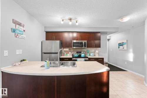 Kitchen with dark wood finish cabinetry, stainless steel appliances, light countertops, decorative backsplash, and light tile patterned floors - 301 10118 106 Avenue, Edmonton, AB - Indoor Photo Showing Kitchen With Double Sink