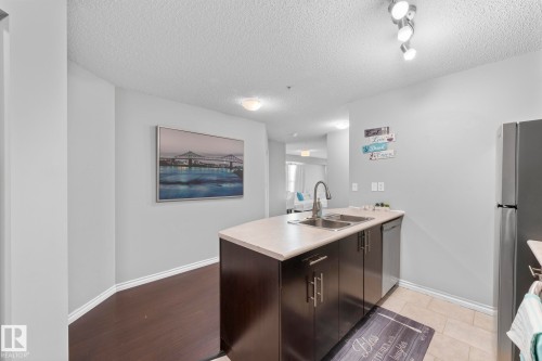 Kitchen featuring a peninsula, light countertops, stainless steel appliances, a textured ceiling, and dark wood finish cabinets - 301 10118 106 Avenue, Edmonton, AB - Indoor Photo Showing Kitchen With Double Sink