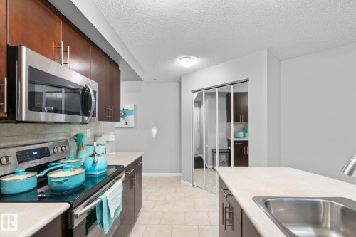 Kitchen with stainless steel appliances, light countertops, tasteful backsplash, a textured ceiling, and dark wood finish cabinets - 301 10118 106 Avenue, Edmonton, AB - Indoor Photo Showing Kitchen