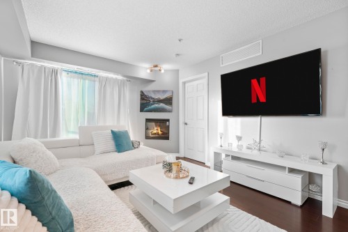 Living room with dark wood-type flooring, a glass covered fireplace, and a textured ceiling - 301 10118 106 Avenue, Edmonton, AB - Indoor Photo Showing Living Room With Fireplace