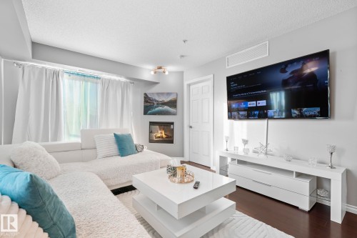 Living room with dark wood-style floors, a glass covered fireplace, and a textured ceiling - 301 10118 106 Avenue, Edmonton, AB - Indoor Photo Showing Living Room With Fireplace