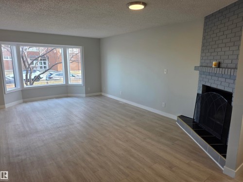 Unfurnished living room with a brick fireplace, light wood-type flooring, and a textured ceiling - Edmonton, AB - Indoor Photo Showing Living Room With Fireplace