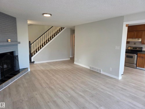 Unfurnished living room featuring a large fireplace, light wood finished floors, and a textured ceiling - Edmonton, AB - Indoor Photo Showing Living Room With Fireplace