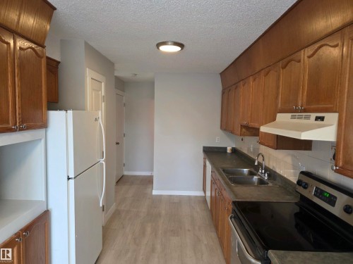 Kitchen featuring stainless steel electric range oven, freestanding refrigerator, wood finish cabinetry, light wood-type flooring, and a textured ceiling - Edmonton, AB - Indoor Photo Showing Kitchen With Double Sink