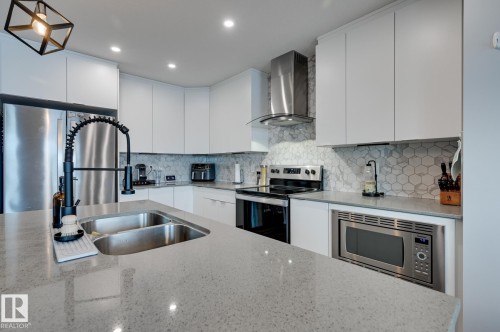 Kitchen featuring modern cabinets, white cabinets, stainless steel appliances, and light stone counters - 4 Caledon Crescent, Spruce Grove, AB - Indoor Photo Showing Kitchen With Stainless Steel Kitchen With Double Sink With Upgraded Kitchen