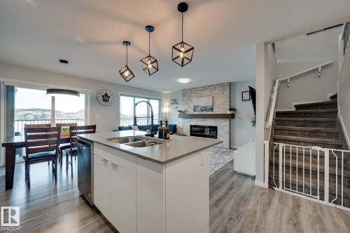 Kitchen featuring white cabinetry, a stone fireplace, hanging light fixtures, and light wood-style floors - 4 Caledon Crescent, Spruce Grove, AB - Indoor Photo Showing Kitchen With Fireplace With Double Sink