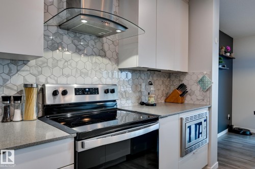 Kitchen featuring stainless steel appliances, island exhaust hood, light stone counters, white cabinetry, and tasteful backsplash - 4 Caledon Crescent, Spruce Grove, AB - Indoor Photo Showing Kitchen With Stainless Steel Kitchen