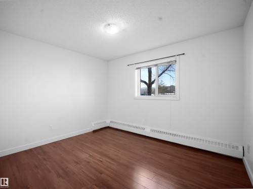 Empty room featuring a baseboard heating unit, dark wood-style flooring, and a textured ceiling - 108 5065 31 Avenue, Edmonton, AB - Indoor Photo Showing Other Room
