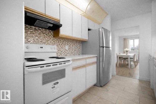 Kitchen featuring electric range, light countertops, exhaust hood, tasteful backsplash, and freestanding refrigerator - 108 5065 31 Avenue, Edmonton, AB - Indoor Photo Showing Kitchen