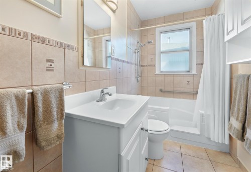 Full bathroom with shower / bath combo with shower curtain, vanity, tile walls, and light tile patterned floors - 11127 71 Avenue, Edmonton, AB - Indoor Photo Showing Bathroom