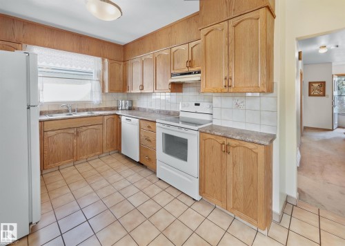 Kitchen featuring white appliances, backsplash, light countertops, light wood finish cabinetry, and light tile patterned flooring - 11127 71 Avenue, Edmonton, AB - Indoor Photo Showing Kitchen With Double Sink