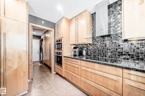 Kitchen with light wood finish cabinetry, dark stone counters, built in refrigerator, a textured ceiling, and black electric stovetop - 4 Harriott Court, St. Albert, AB - Indoor Photo Showing Kitchen