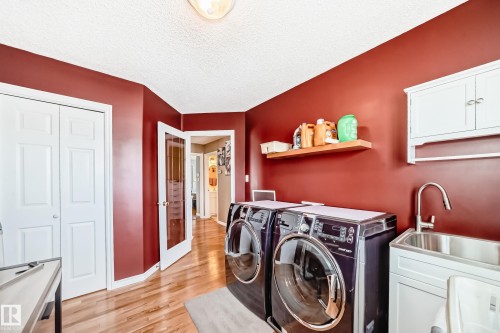 Laundry room featuring light wood-style flooring, cabinet space, washer and clothes dryer, and a textured ceiling - 4 Harriott Court, St. Albert, AB - Indoor Photo Showing Laundry Room