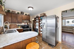 Kitchen with stainless steel fridge with ice dispenser, range with electric stovetop, light countertops, dark wood finish cabinets, and a peninsula - 