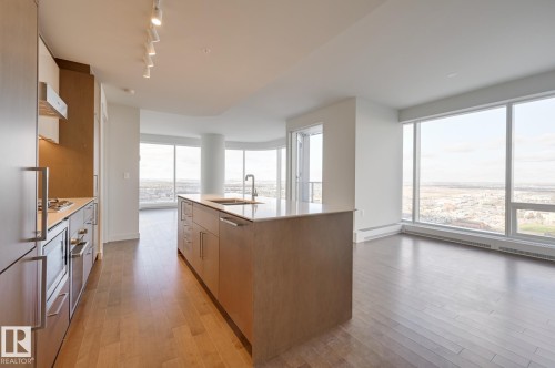 Kitchen featuring a kitchen island with sink, light stone counters, track lighting, light wood-style floors, and brown cabinets - 3901 10360 102 Street, Edmonton, AB - Indoor Photo Showing Kitchen With Upgraded Kitchen