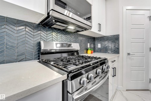 Kitchen with stainless steel appliances, light stone countertops, white cabinets, decorative backsplash, and light marble finish floors - 1522 17 Avenue, Edmonton, AB - Indoor Photo Showing Kitchen