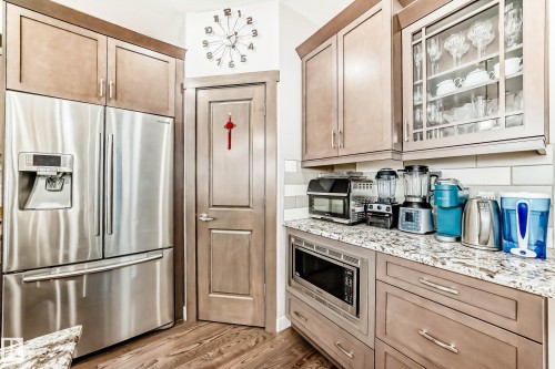 Kitchen with stainless steel appliances, light stone counters, light wood-style flooring, and glass insert cabinets - 7719 Getty Wynd, Edmonton, AB - Indoor Photo Showing Kitchen