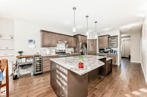 Kitchen with light stone counters, an island with sink, pendant lighting, beverage cooler, and light wood finished floors - 7719 Getty Wynd, Edmonton, AB - Indoor Photo Showing Kitchen With Upgraded Kitchen