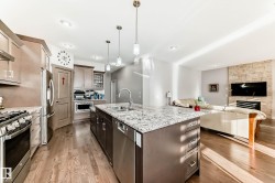 Two tone kitchen featuring pendant lighting, stainless steel appliances, an island with sink, light stone counters, and open floor plan - 
