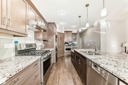 Dual tone kitchen featuring stainless steel appliances, decorative light fixtures, light wood finished floors, light stone countertops, and two tone cabinetry - 