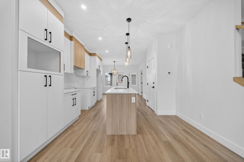 Two tone kitchen with two tone cabinets, suspended lighting, a center island with sink, light wood-style flooring, and light stone countertops - 436 Crystal Creek Link, Leduc, AB - Indoor