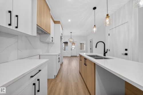 Kitchen with two tone cabinetry, modern cabinets, hanging light fixtures, light wood-style floors, and light stone counters - 436 Crystal Creek Link, Leduc, AB - Indoor Photo Showing Kitchen With Double Sink With Upgraded Kitchen