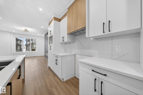 Kitchen featuring two tone cabinetry, light wood-style flooring, light stone counters, recessed lighting, and modern cabinets - 436 Crystal Creek Link, Leduc, AB - Indoor Photo Showing Kitchen With Double Sink