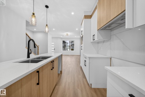 Kitchen with two tone cabinetry, light stone counters, light wood-style flooring, hanging light fixtures, and modern cabinets - 436 Crystal Creek Link, Leduc, AB - Indoor Photo Showing Kitchen With Double Sink