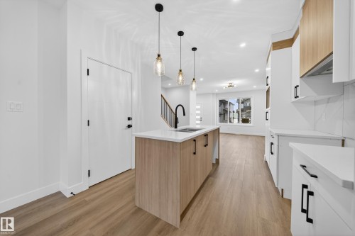 Kitchen with two tone cabinets, light stone countertops, a kitchen island with sink, light wood-style floors, and pendant lighting - 436 Crystal Creek Link, Leduc, AB - Indoor Photo Showing Kitchen