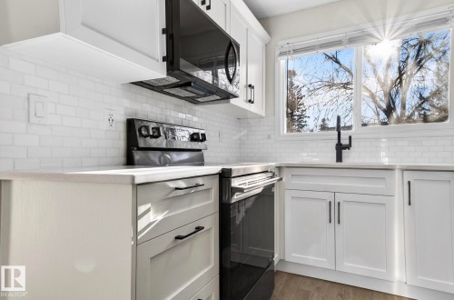 Kitchen featuring black / electric stove, white cabinets, light stone counters, light wood-type flooring, and tasteful backsplash - 9969 171 Ave, Edmonton, AB - Indoor Photo Showing Kitchen
