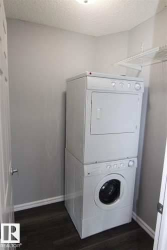 Laundry room featuring stacked washer and clothes dryer, dark wood finished floors, and a textured ceiling - 404 4407 23 Street, Edmonton, AB - Indoor Photo Showing Laundry Room