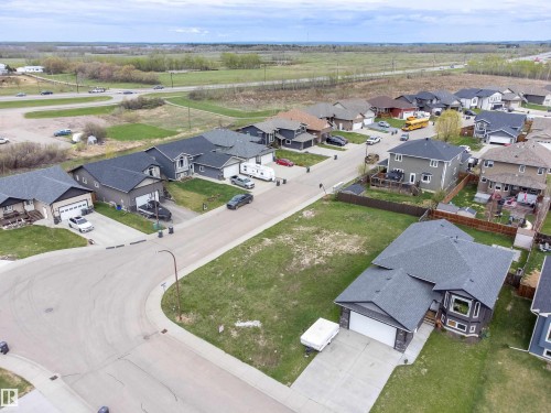Expansive corner lot featuring a partial concrete driveway, dark gray shingle roof, and a bay window with stone accents - 4930 57 Avenue, Cold Lake, AB 
