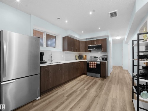 Kitchen featuring stainless steel appliances, light countertops, dark wood finish cabinetry, light wood-style flooring, and tasteful backsplash - 5423 Chappelle Road, Edmonton, AB - Indoor Photo Showing Kitchen