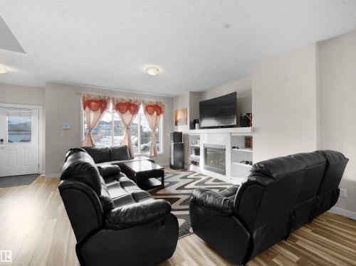 Living area featuring light wood finished floors, a glass covered fireplace, and a textured ceiling - 5423 Chappelle Road, Edmonton, AB - Indoor Photo Showing Living Room