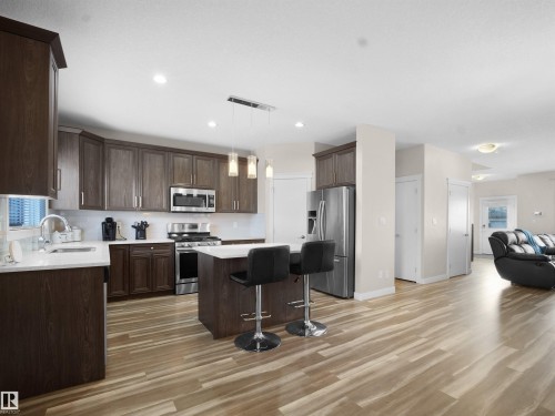 Kitchen featuring stainless steel appliances, a kitchen bar, decorative light fixtures, a center island, and dark wood finish cabinets - 5423 Chappelle Road, Edmonton, AB - Indoor Photo Showing Kitchen With Upgraded Kitchen