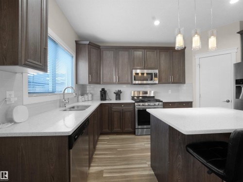 Kitchen with dark wood finish cabinetry, stainless steel appliances, a breakfast bar area, light stone countertops, and tasteful backsplash - 5423 Chappelle Road, Edmonton, AB - Indoor Photo Showing Kitchen With Double Sink With Upgraded Kitchen