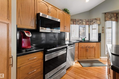 Kitchen featuring stainless steel appliances, light wood finished floors, wood finish cabinets, lofted ceiling, and decorative backsplash - 519 Buchanan Road, Edmonton, AB - Indoor Photo Showing Kitchen