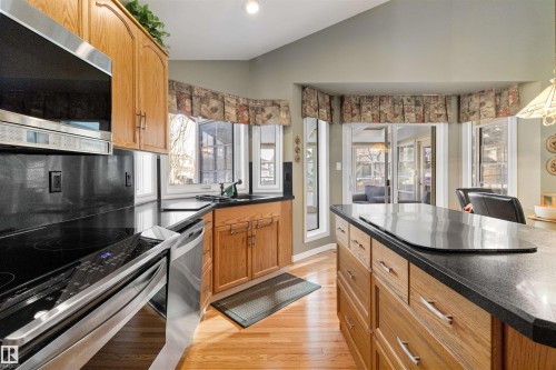 Kitchen featuring stainless steel appliances, vaulted ceiling, wood finish cabinetry, light wood-type flooring, and dark stone countertops - 519 Buchanan Road, Edmonton, AB - Indoor Photo Showing Kitchen
