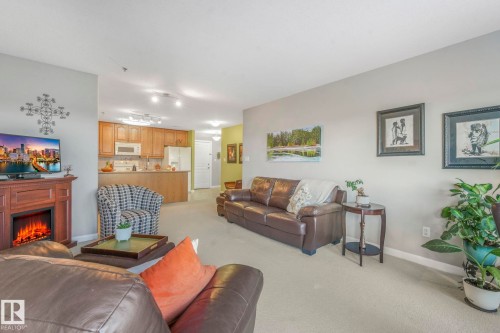 Living area featuring a lit fireplace and light carpet - 415 530 Hooke Road, Edmonton, AB - Indoor Photo Showing Living Room With Fireplace