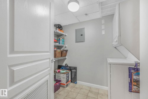 Laundry room with stacked washer / drying machine, a paneled ceiling, electric panel, and light tile patterned floors - 415 530 Hooke Road, Edmonton, AB - Indoor