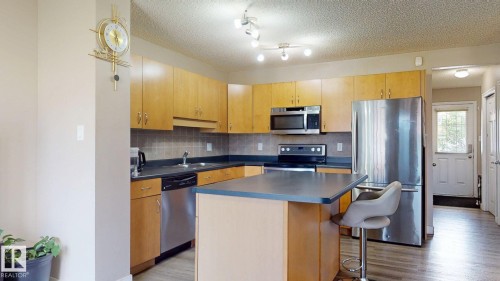 Kitchen featuring stainless steel appliances, a kitchen island, a kitchen breakfast bar, a textured ceiling, and dark countertops - 1150 37B Avenue, Edmonton, AB - Indoor Photo Showing Kitchen With Stainless Steel Kitchen