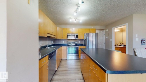 Kitchen with dark countertops, stainless steel appliances, a kitchen island, a textured ceiling, and light wood-type flooring - 1150 37B Avenue, Edmonton, AB - Indoor Photo Showing Kitchen With Stainless Steel Kitchen With Double Sink