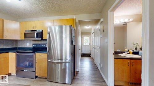Kitchen featuring stainless steel appliances, dark countertops, a textured ceiling, tasteful backsplash, and light wood finished floors - 1150 37B Avenue, Edmonton, AB - Indoor Photo Showing Kitchen